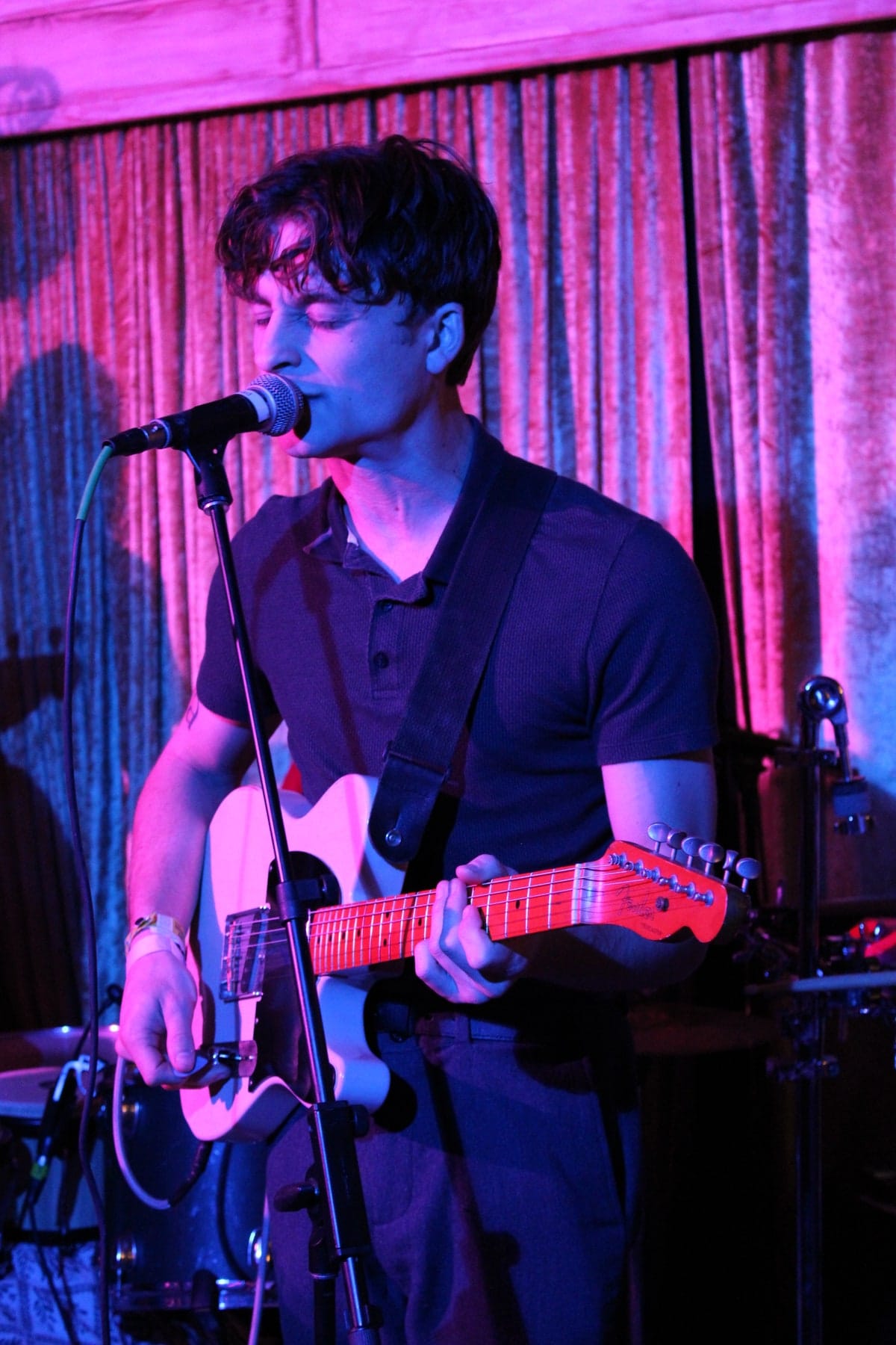 A musician sings and plays guitar under blue and pink lighting.
